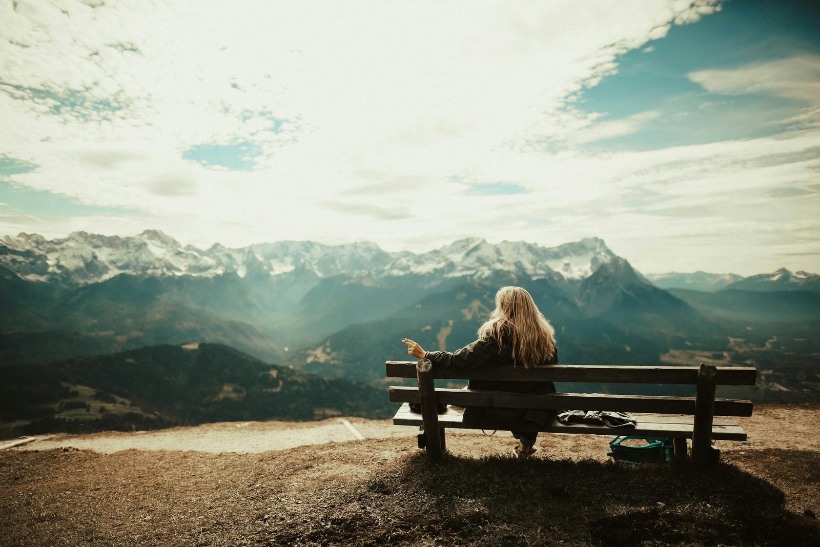 Woman enjoys a peaceful view of snow-capped mountains from a bench, capturing the essence of nature's serenity.