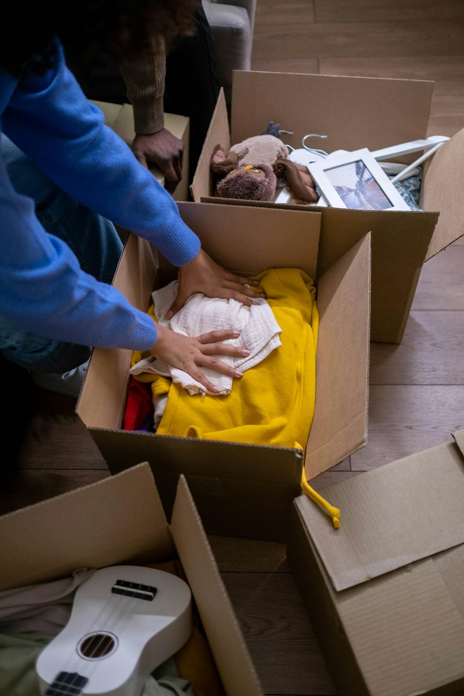 People organizing clothes and toys into cardboard boxes for moving or storage.