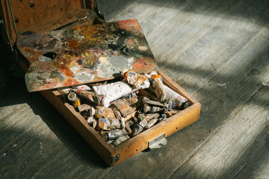 Close-up of a wooden paint set with colorful tubes and palette on a textured floor.
